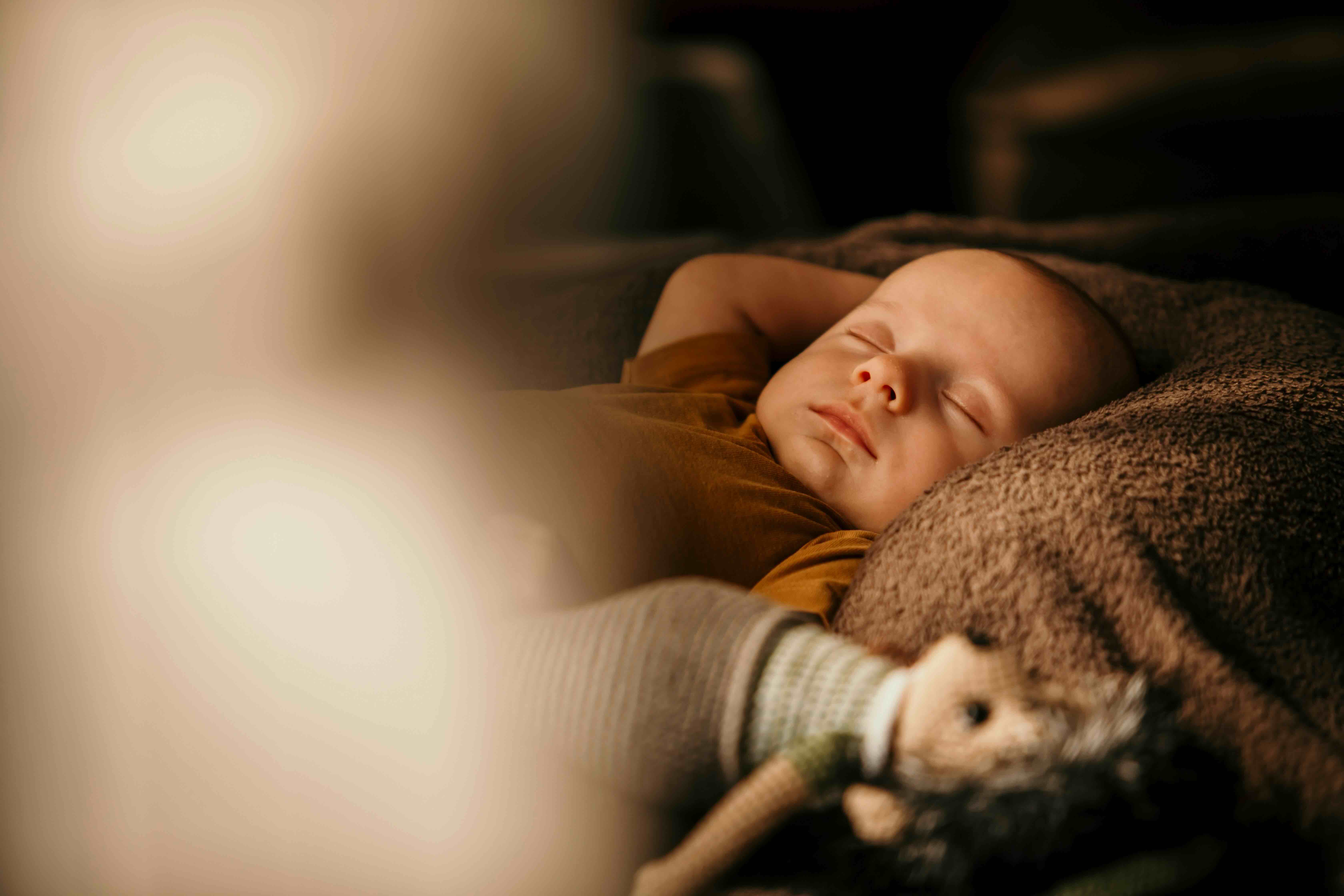 Bébé profondément endormi, les poings en l'air et un doudou tout près – une image de sommeil paisible, serein, retrouvé.