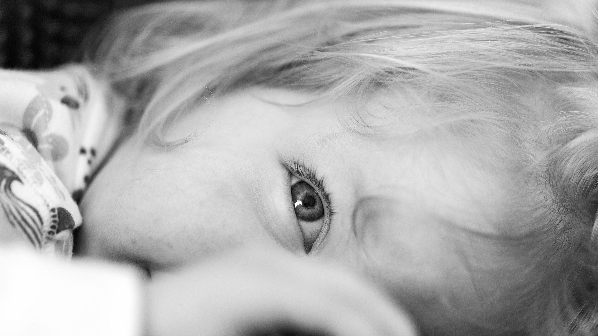 Petite fille allongée sur le ventre, regard malicieux ; image en noir et blanc illustrant une évolution positive du sommeil vers plus d'autonomie