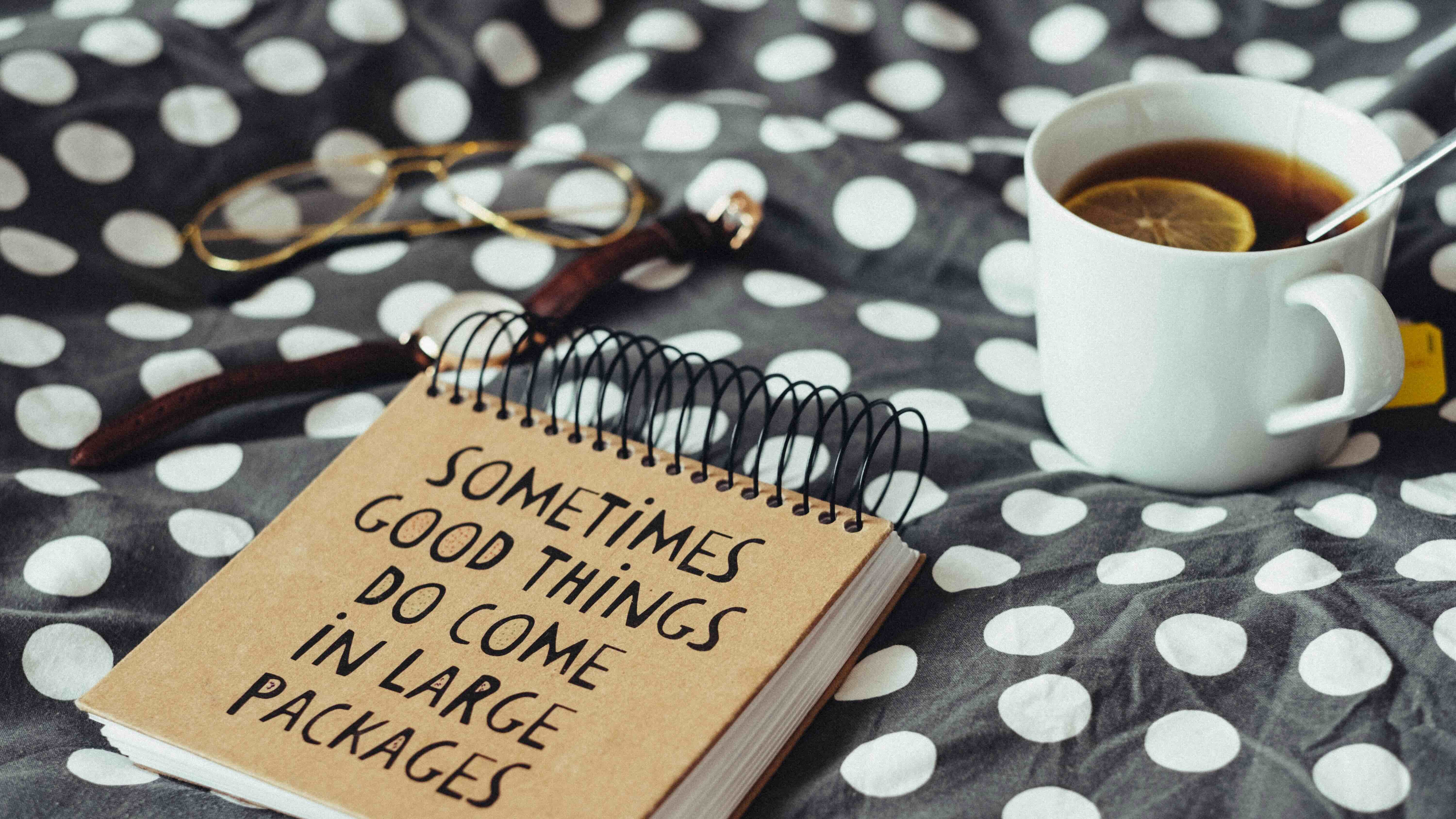 Carnet kraft avec le message "sometimes good things do come in large packages", posé sur un plaid, à côté d'une tasse de thé – illustration du cheminement d'Émeline et Rémi après un accompagnement sommeil respectueux pour leur bébé allaité.