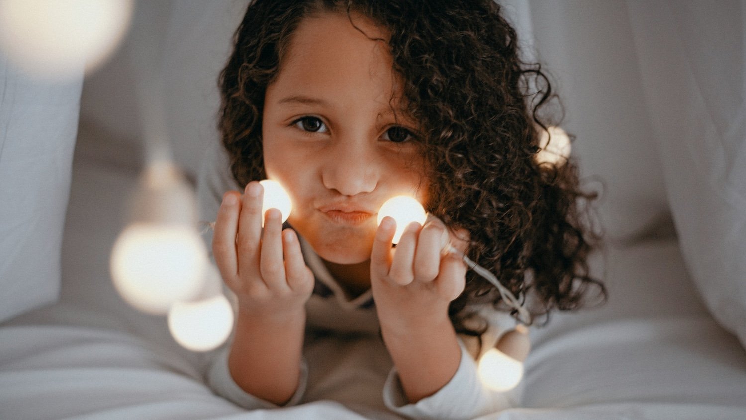 Petite fille de 3 ans qui joue dans son lit cabane avec une guirlande avant de dormir, coucher compliqué qui évoque les difficultés de sommeil liées à l'entrée à l'école