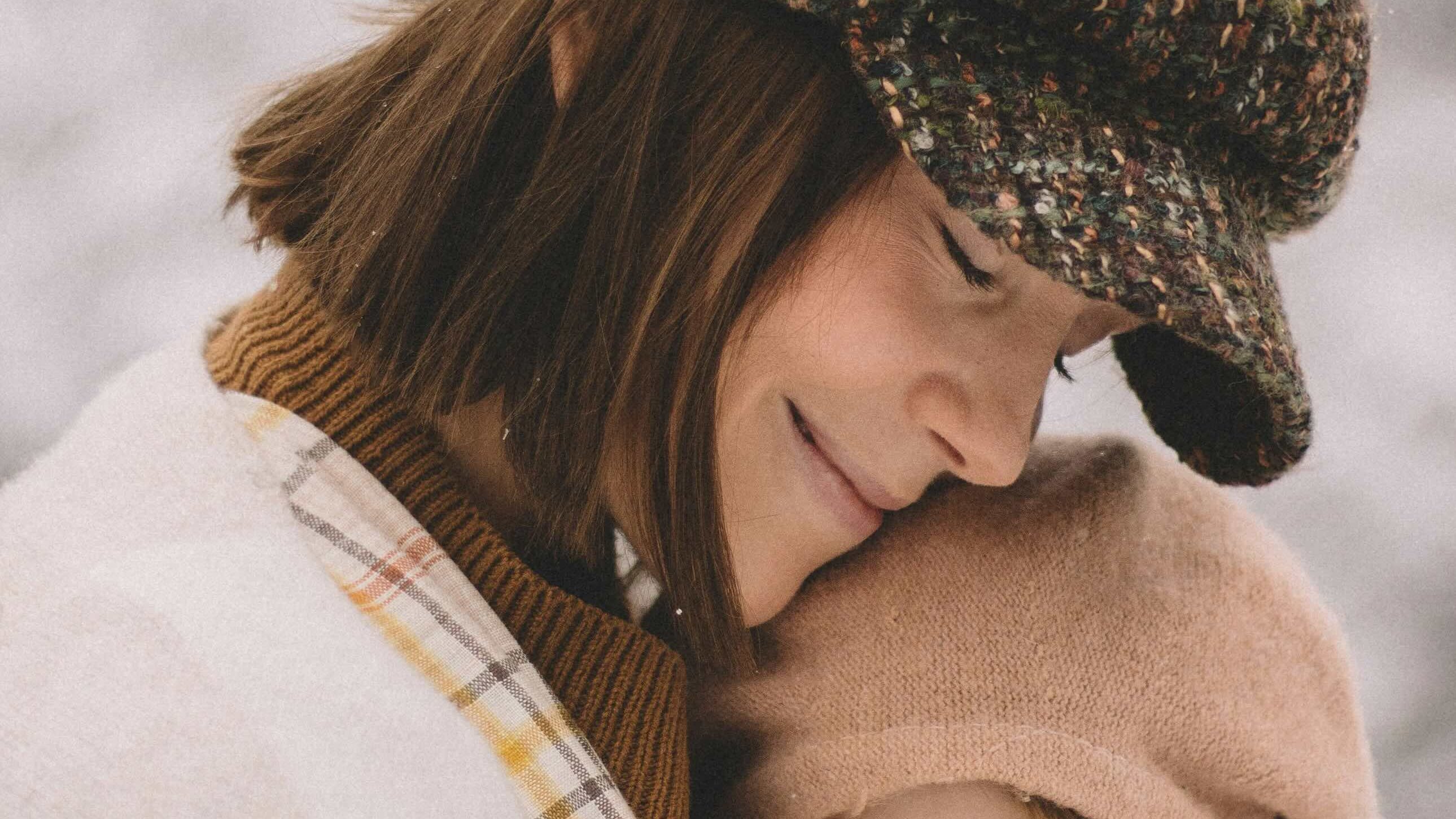 Maman souriante en manteau d'hiver câlinant son bébé en porte-bébé, moment doux et complice
