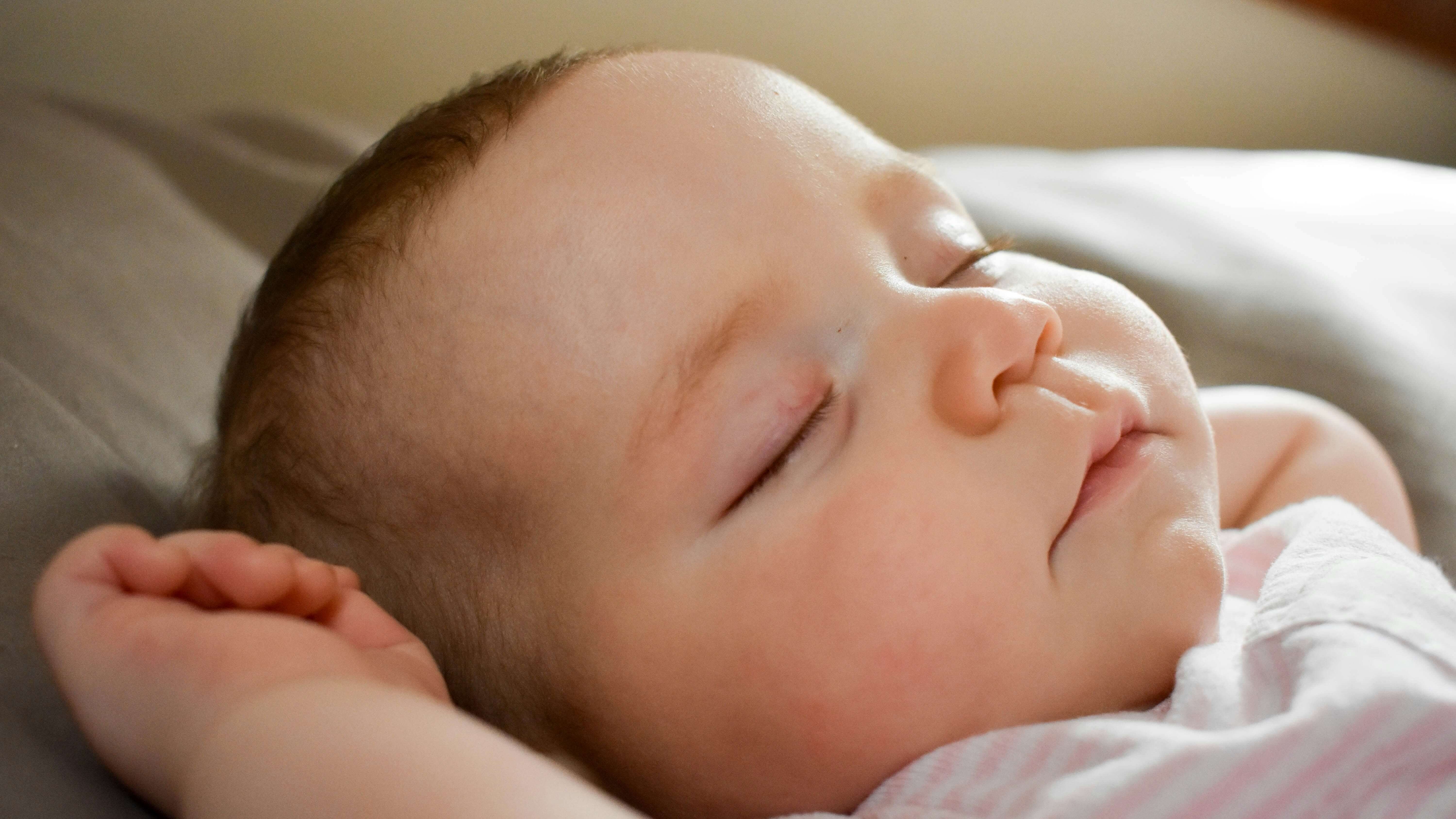 Gros plan visage d'un bébé endormi profondément, poings fermés près du visage, symbole de sommeil paisible et naturel chez les nourrissons