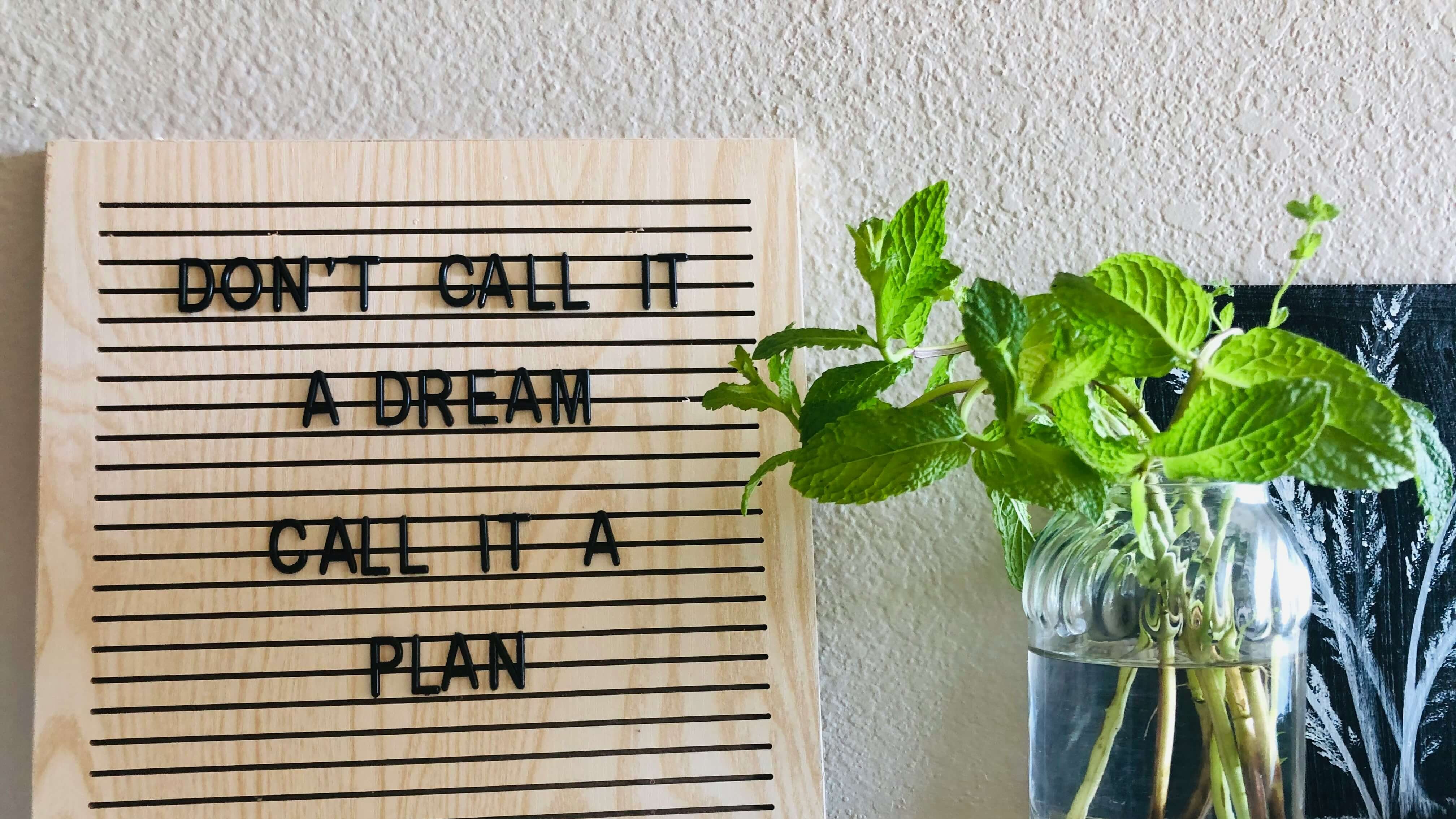 Citation inspirante "Don't call it a dream, call it a plan" posée sur un bureau avec une plante, symbolisant la préparation et l'engagement dans l'accompagnement du sommeil des enfants