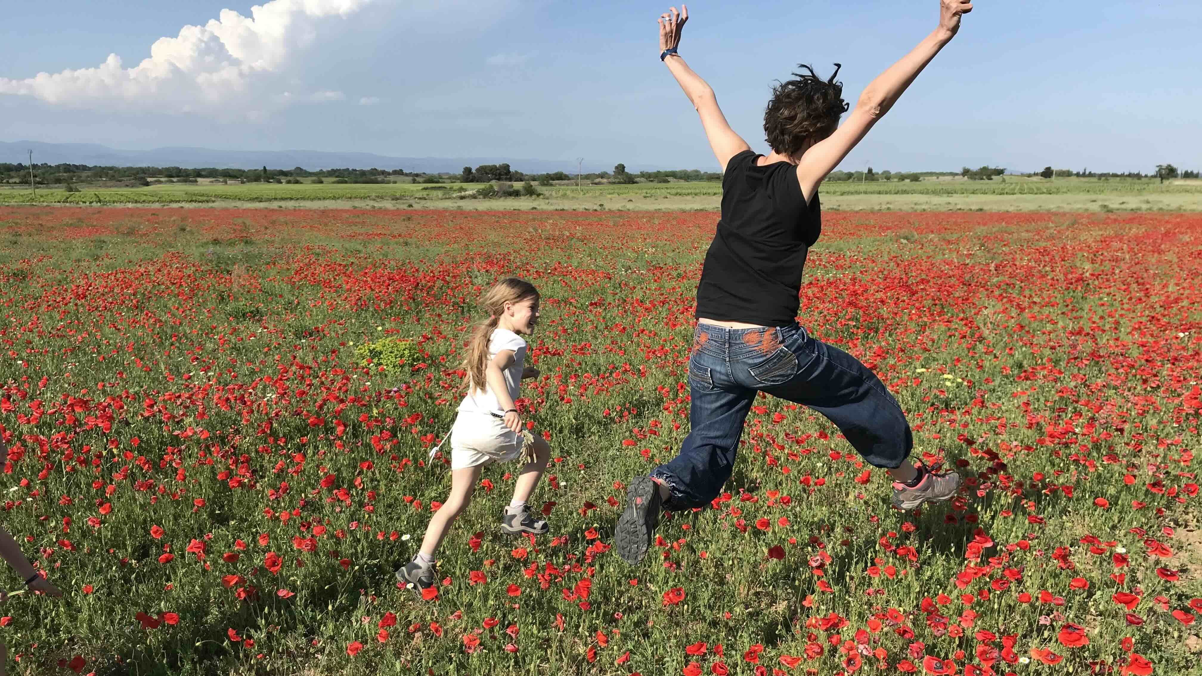Lucie Perrin, consultante sommeil, et sa fille de dos, courant et sautant dans un champ de coquelicots, symbolisant la joie, l'énergie et un nouveau départ