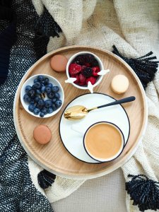 Plateau en bois vu du dessus avec café crème, bol de myrtilles, bol de framboises et macarons – pause gourmande au Pompon sur la Daronne à Toulouse.