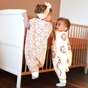 2 enfants souriants d'environ 18 mois portant des giboteuses à pieds et escaladant leur lit à barreau