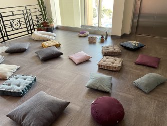 Atelier collectif sommeil bébé avec coussins au sol, salle lumineuse et ensoleillée, favorisant confort et détente pour les parents et jeunes enfants