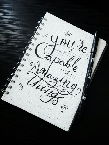 Message 'You're capable of amazing things' écrit au crayon noir sur un carnet blanc — symbole d'encouragement dans l'accompagnement sommeil d'une maman fatiguée.