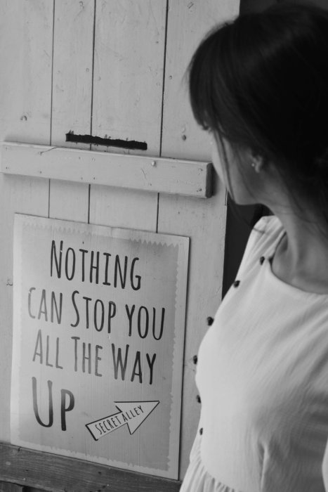 Femme de profil regardant un panneau noir et blanc avec message « nothing can't stop you all the way up » — métaphore d'un parcours vers l'autonomie et la confiance, en lien avec l'accompagnement sommeil de bébé.