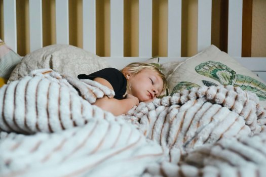 Enfant paisiblement endormi dans un lit de grand — symbole de nuits enfin retrouvées pour toute la famille.