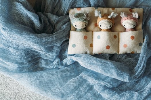 Trois petits doudous rangés dans un vide-poche pour lit bébé, textile lange bleu doux, ambiance chambre apaisante pour bébé.