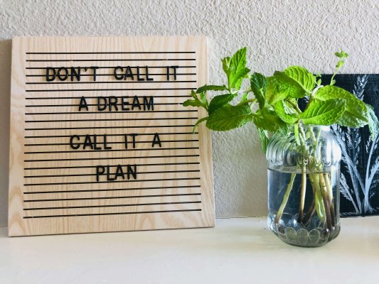 Citation inspirante "Don't call it a dream, call it a plan" posée sur un bureau avec une plante, symbolisant la préparation et l'engagement dans l'accompagnement du sommeil des enfants