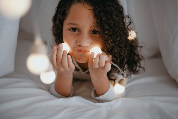 Petite fille de 3 ans qui joue dans son lit cabane avec une guirlande avant de dormir, coucher compliqué qui évoque les difficultés de sommeil liées à l'entrée à l'école
